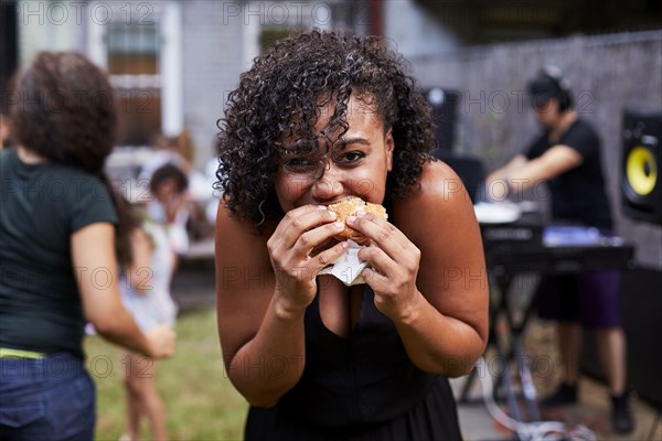 Mixed Race woman eating hamburger at backyard party