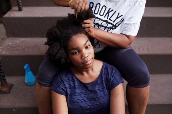 Black mother styling hair of daughter on staircase