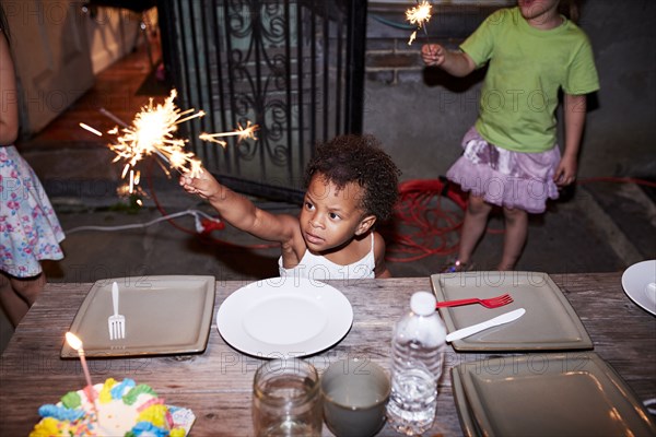 Serious girl holding burning sparkler at backyard party