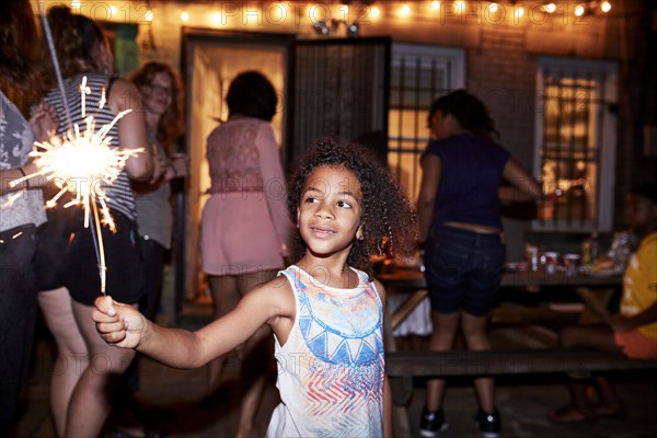 Smiling girl holding burning sparkler at backyard party