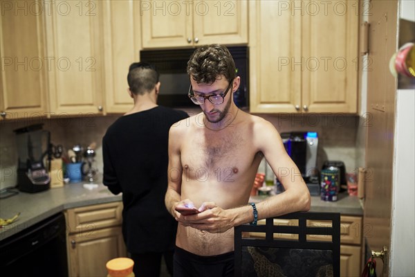 Man with bare chest texting on cell phone in kitchen