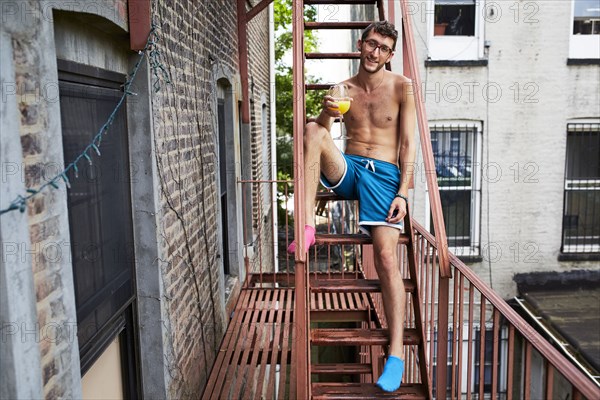 Caucasian man sitting on urban fire escape drinking orange juice