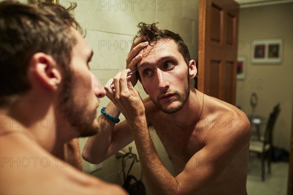 Reflection of Caucasian man plucking eyebrow in mirror