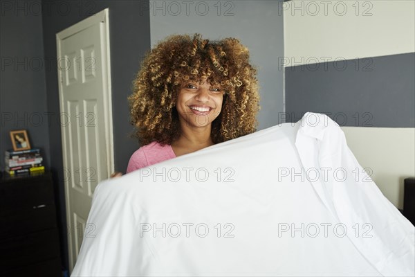 Black woman holding sheet in bedroom