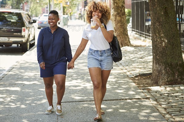 Black women holding hands on city sidewalk