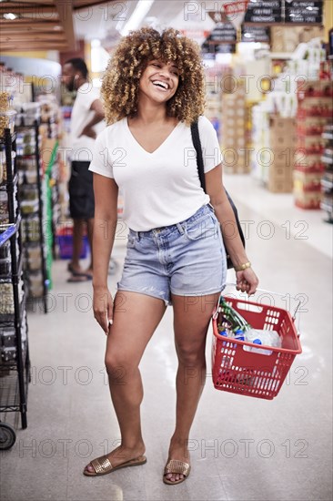 Smiling Black woman holding basket in grocery store