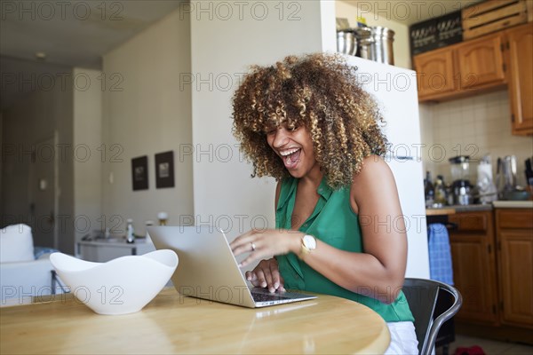 Laughing Black woman using laptop at table