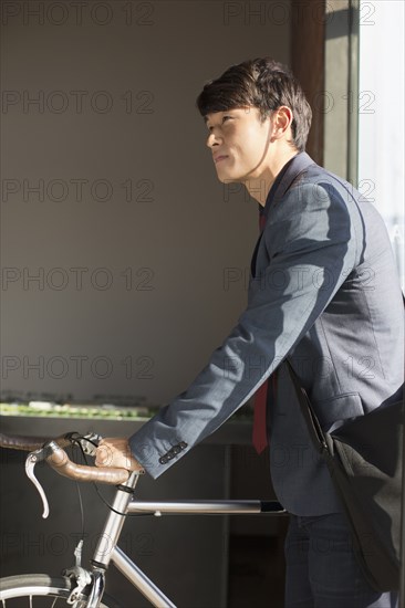 Korean businessman wheeling bicycle in office