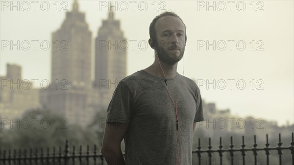 Caucasian runner listening to earbuds in front of city skyline