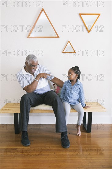 African American grandfather pointing at granddaughter on bench