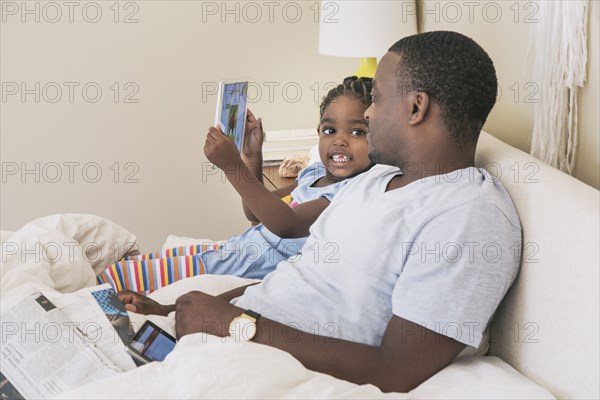 African American father and daughter using digital tablet on bed