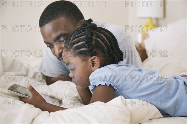 African American father and daughter using digital tablet on bed