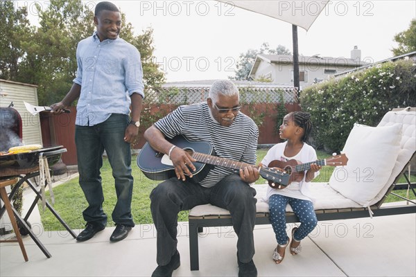 African American grandfather teaching granddaughter to play guitar