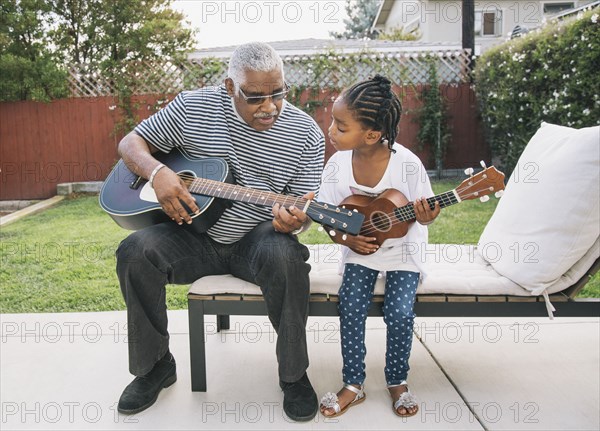 African American grandfather teaching granddaughter to play guitar