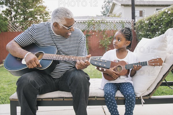 African American grandfather teaching granddaughter to play guitar