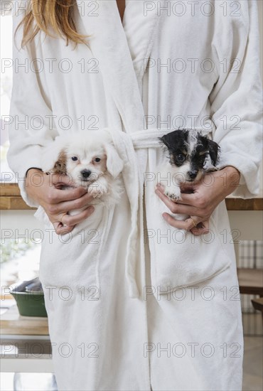 Caucasian woman wearing bathrobe carrying puppies in pockets