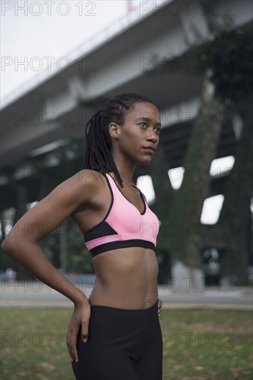 Serious Mixed Race woman wearing pink sports-bra near bridge