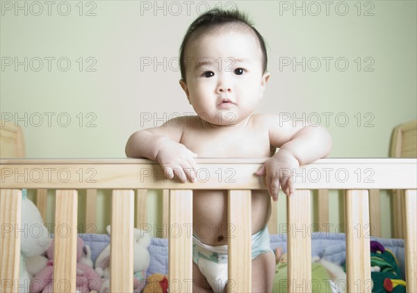 Asian baby standing in crib