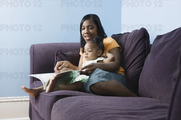 African mother reading to young daughter on sofa