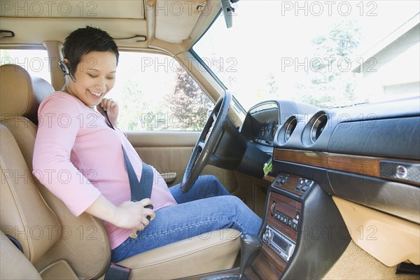 Pregnant woman putting on seatbelt in car