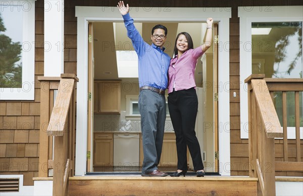 Asian couple waving in front of new house