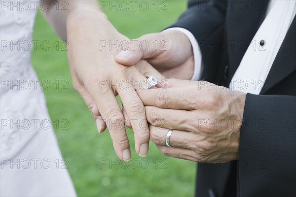 Asian groom putting ring on bride's finger