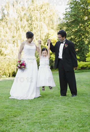 Asian newlyweds holding flower girl's hands