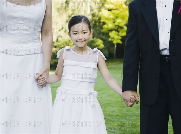 Asian newlyweds holding flower girl's hands