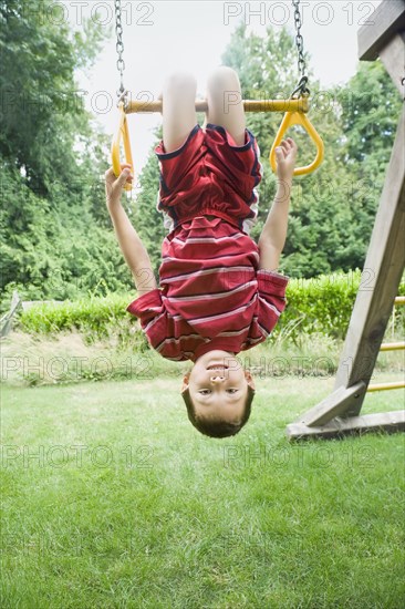 Asian boy hanging upside down on play structure