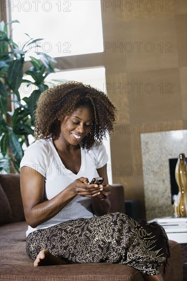 African woman text messaging on cell phone in living room