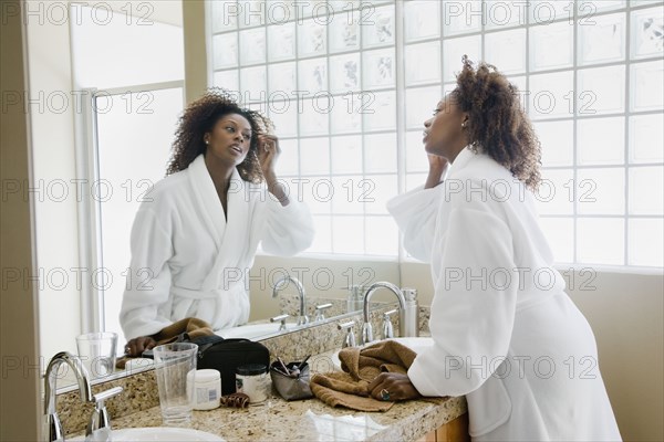 African woman putting on makeup in bathroom