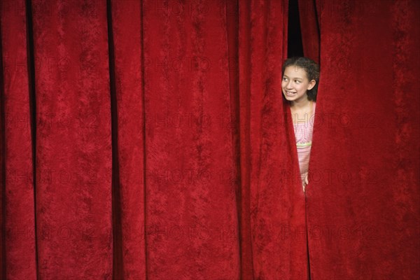 Mixed race person hiding behind stage curtain