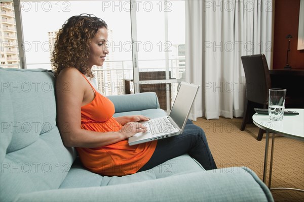 Hispanic woman using laptop on sofa