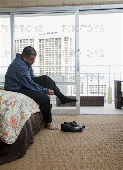 Mixed race man putting socks and shoes on at end of bed