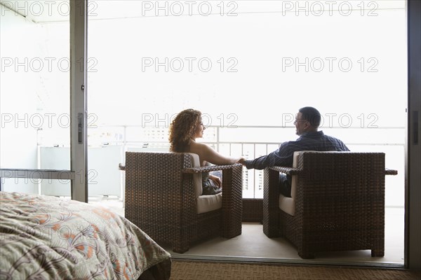 Couple sitting in armchairs and holding hands on urban balcony