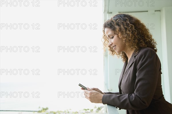 Hispanic woman text messaging on balcony