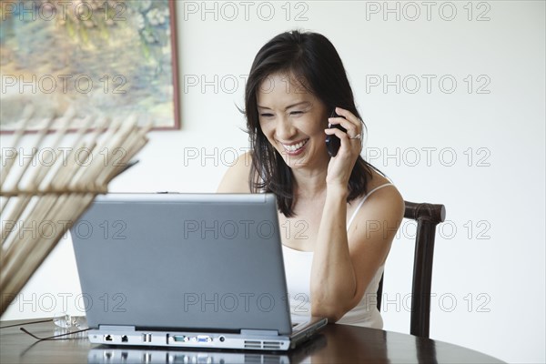 Japanese woman using laptop and talking on cell phone