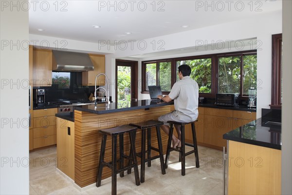 Japanese man using laptop at kitchen counter