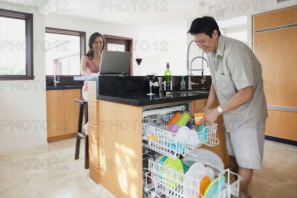 Japanese man doing dishes while woman uses laptop