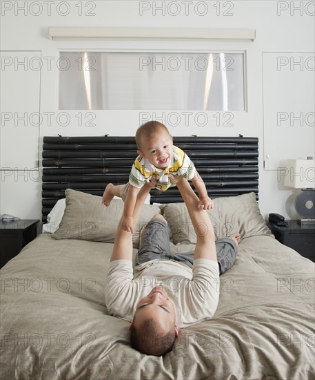 Father lifting son on bed in bedroom