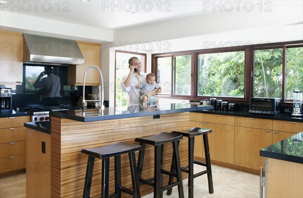 Father holding son and talking on phone in kitchen