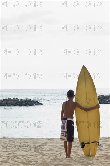 Mixed race boy on beach with surfboard