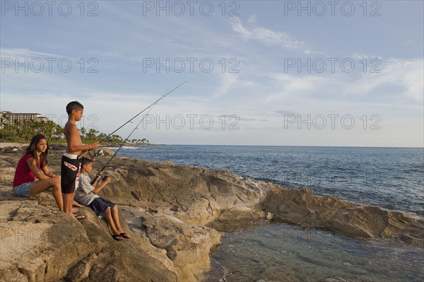 Mixed race children fishing in ocean