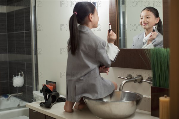 Mixed race girl on counter putting on lipstick