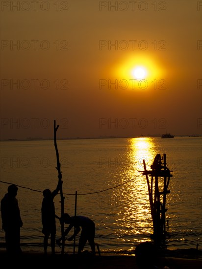 Silhouettes of men standing near river at sunset