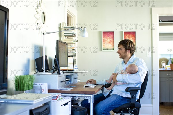 Caucasian father working in home office and holding baby