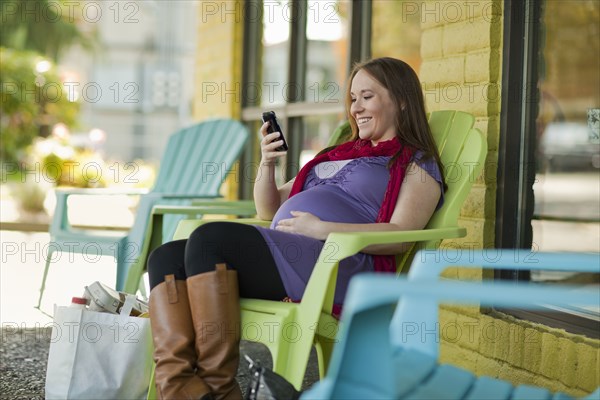 Pregnant Caucasian woman text messaging outdoors