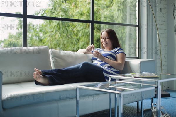 Pregnant Caucasian woman eating on sofa