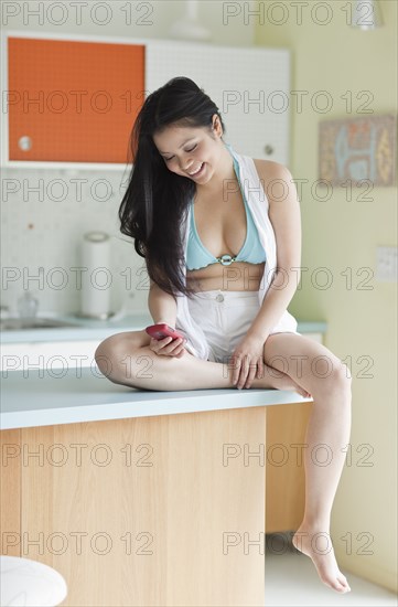 Vietnamese woman sitting on counter text messaging
