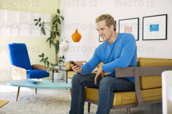 Caucasian man text messaging on cell phone in living room